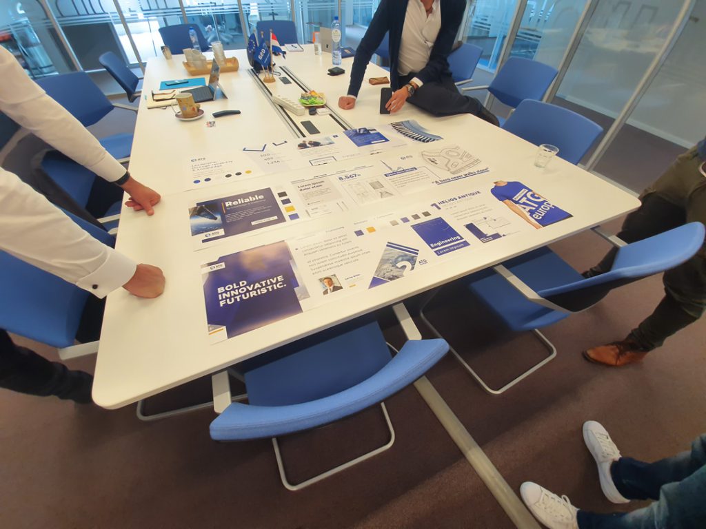 Business professionals reviewing marketing materials and company branding elements on conference table in a corporate meeting room.